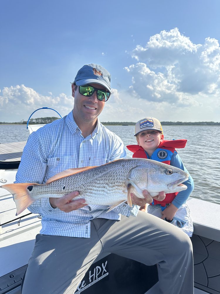 Father and young son in a life jacket holding a redfish