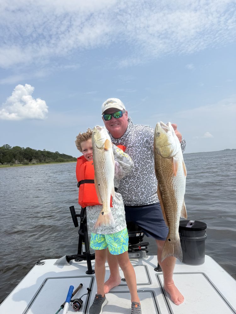 Father and son each holding a redfish on the bow