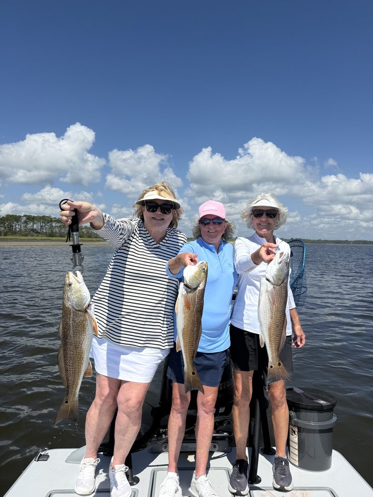 Three anglers on the bow each holding a redfish