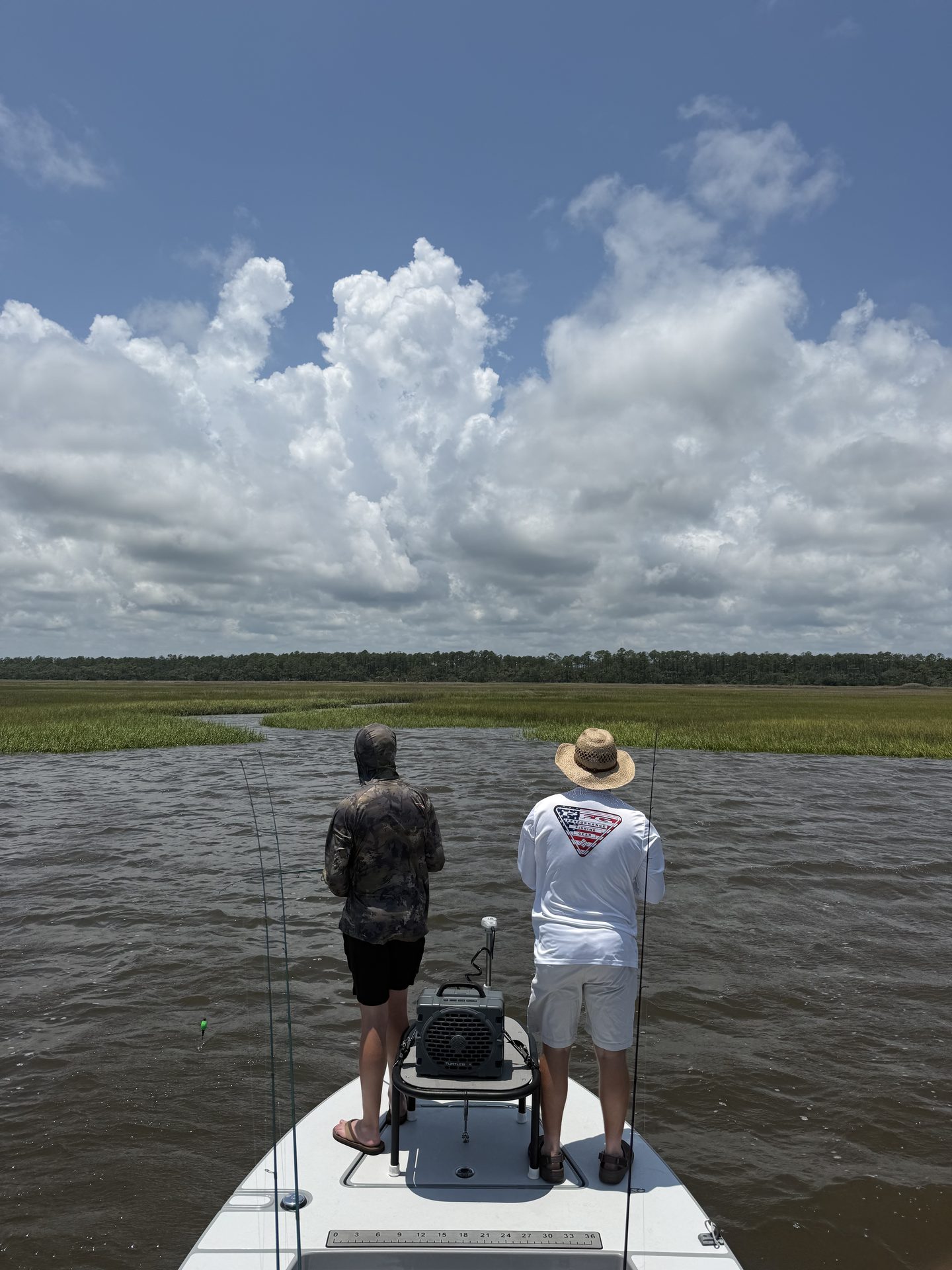 Two anglers casting from the bow of the skiff toward the marsh
