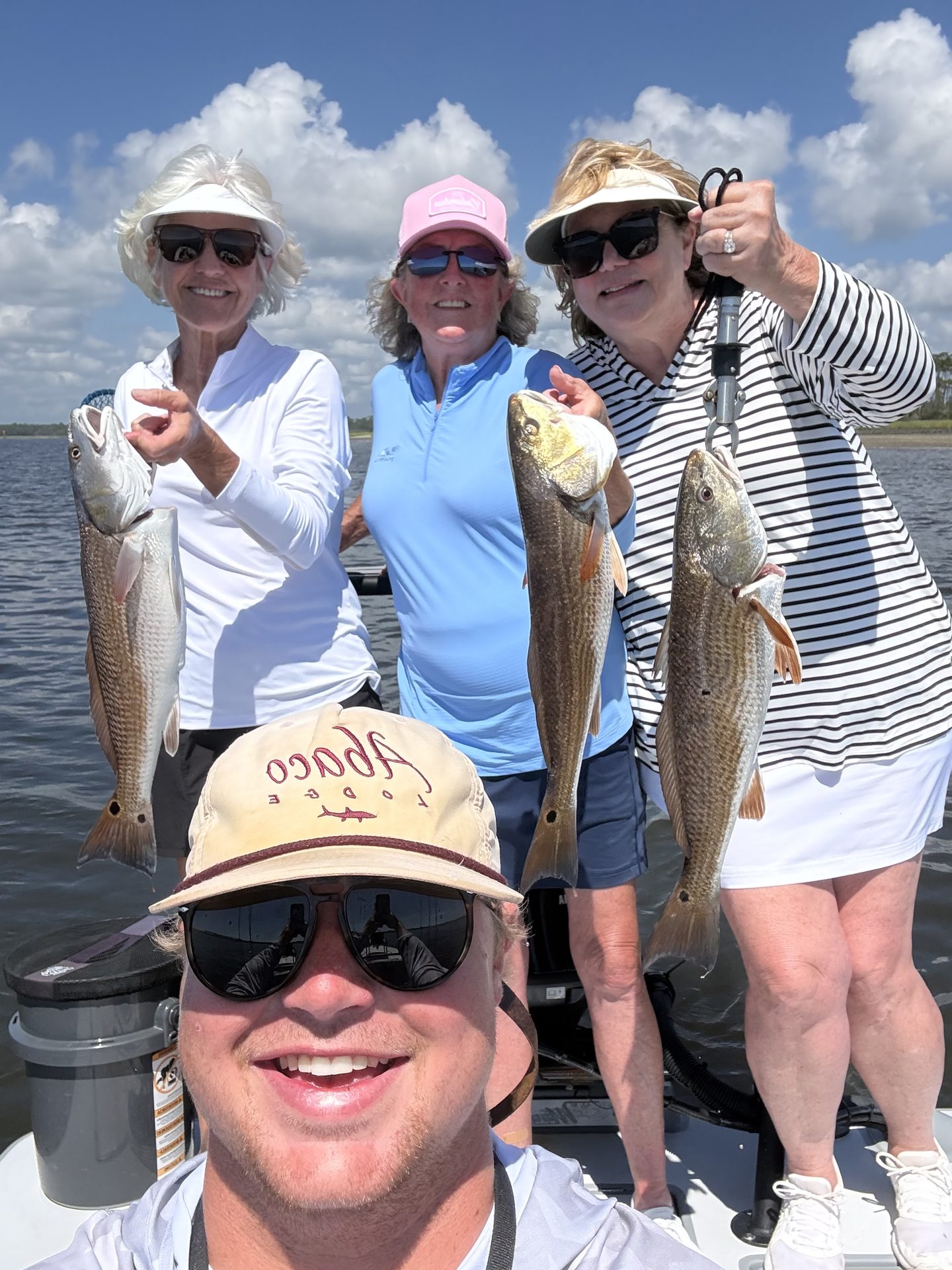 Captain Wills Hardegree taking a selfie on the skiff with three smiling clients, each holding a redfish